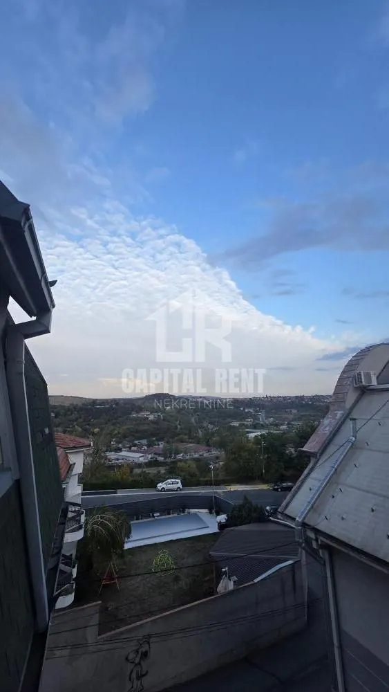 Pogled iz visine na naselje, parking i okolni pejzaž.