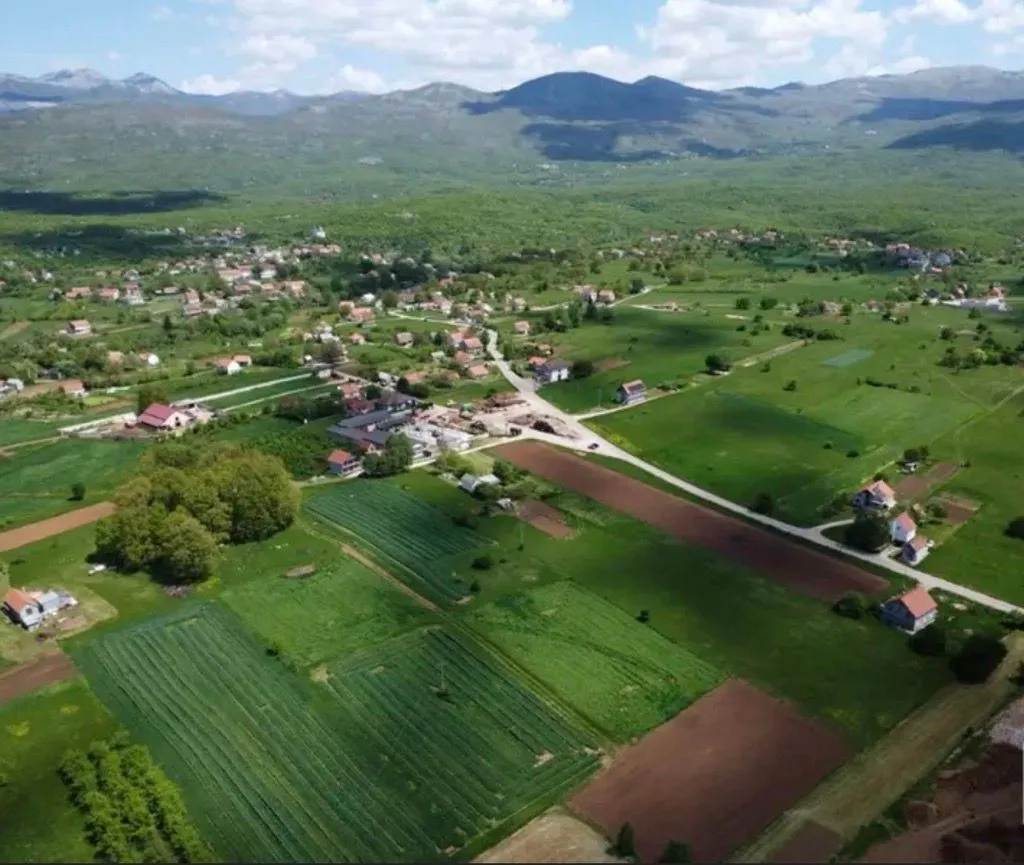 Pogled iz vazduha na seosko imanje sa okolnim poljima i planinama.