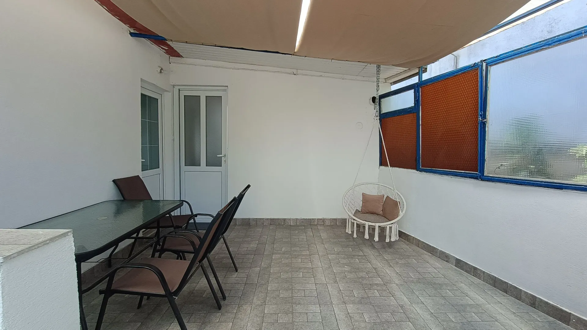 Natkrivena terasa sa garniturom za sjedenje i visećom stolicom.