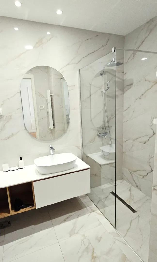 Modernly equipped bathroom with a washbasin and a walk-in shower tiled with marble-effect ceramics.