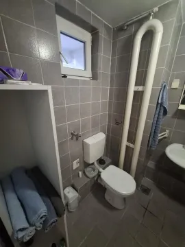 Manje kupatilo obloženo sivim pločicama sa wc šoljom, umivaonikom i policom za peškire. - image 9