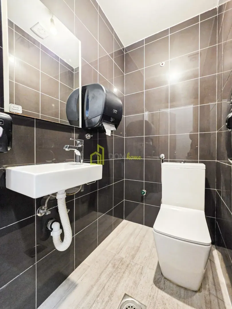 Small bathroom lined with dark tiles featuring a washbasin and a toilet.