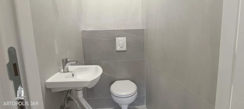 Manje kupatilo sa umivaonikom i wc šoljom obloženo sivim pločicama.