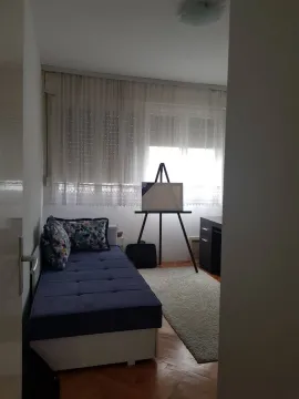A small bedroom with a blue bed, a desk, and an easel by the window. - image 9