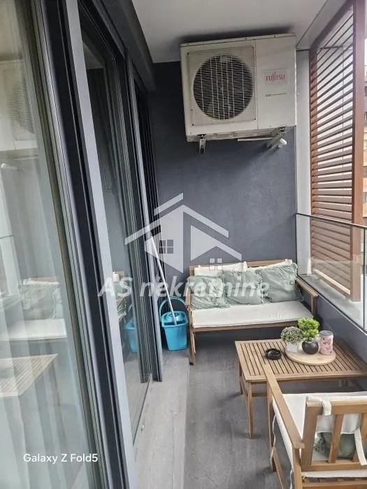 Small furnished balcony with seating furniture and an outdoor air conditioning unit.