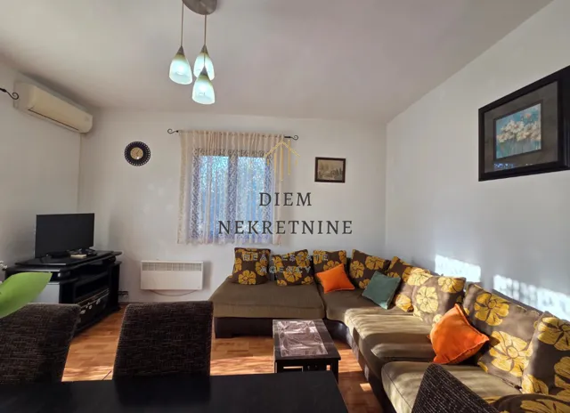 Dnevna soba sa garniturom za sedenje, televizorom i trpezarijskim stolom.