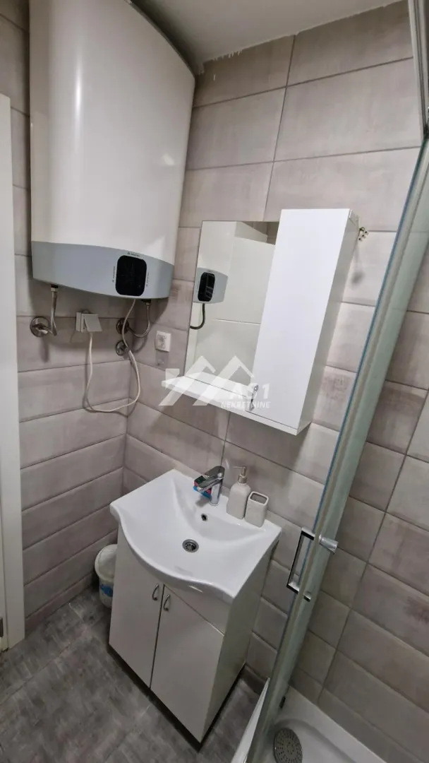 Manje kupatilo sa umivaonikom, ogledalom, bojlerom i tuš kabinom.
