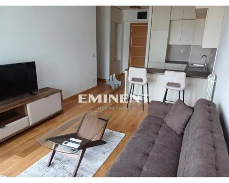 Living room with a sofa, TV, and kitchen in the background. - image 2