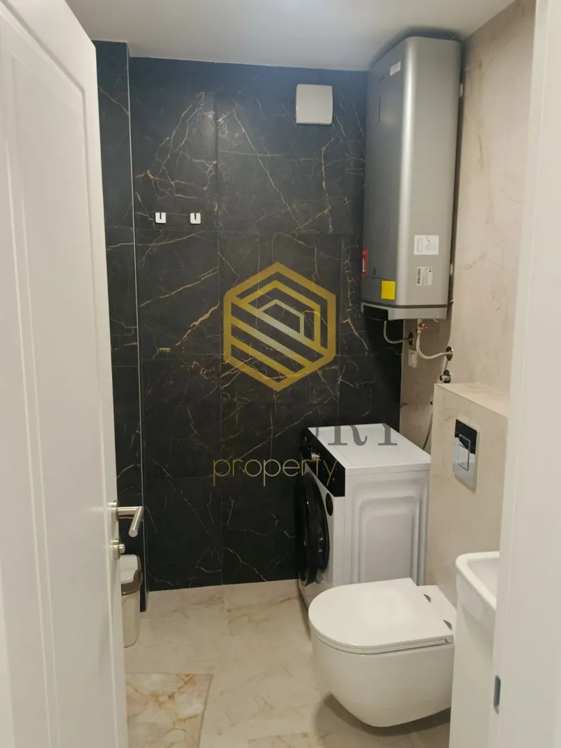 Smaller bathroom with a toilet, washing machine, and dark marble tiles.