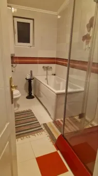 Bathroom equipped with a bathtub, shower cabin, toilet, and a small window. - image 5