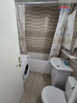 Compact bathroom with a bathtub, washbasin, toilet, and washing machine. - image 12