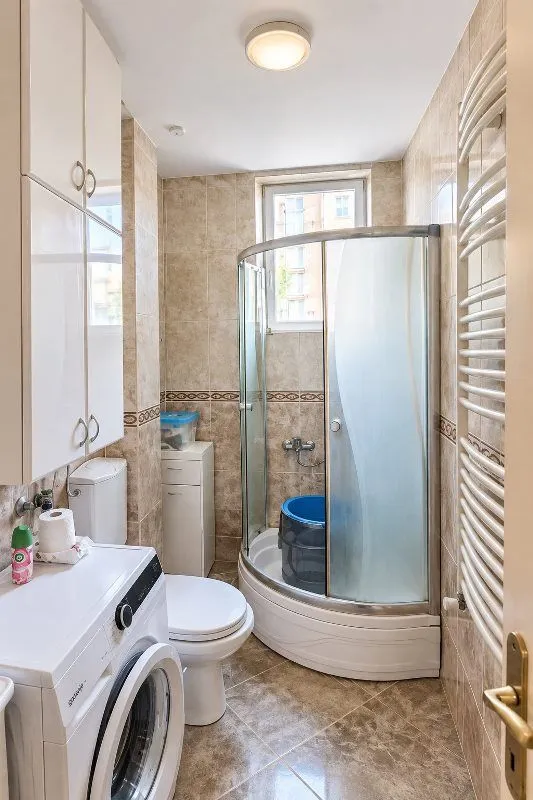 Compact bathroom with a shower cabin, toilet, and washing machine.