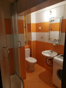 Bathroom with orange and white tiles, a shower cabin, and a washing machine. - image 6