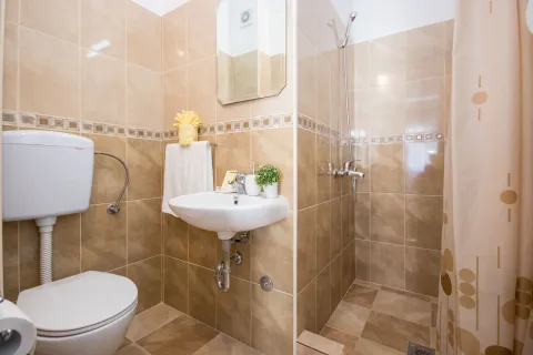 Compact bathroom tiled in beige with a washbasin, toilet, and shower area. - image 11