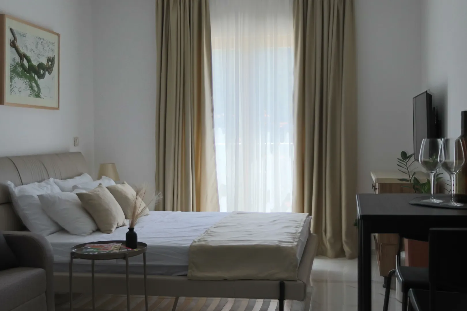 A furnished bedroom with a double bed and a window with light curtains.