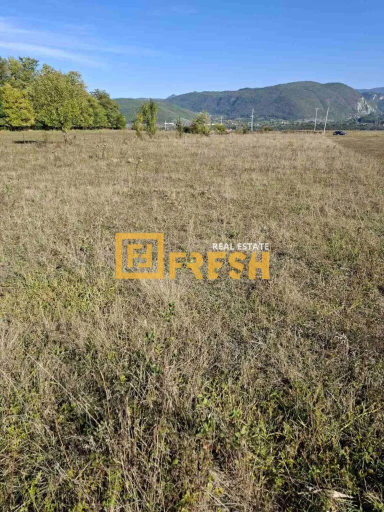 Pogled na prostrano zemljište sa travnatom površinom i planinama u pozadini.