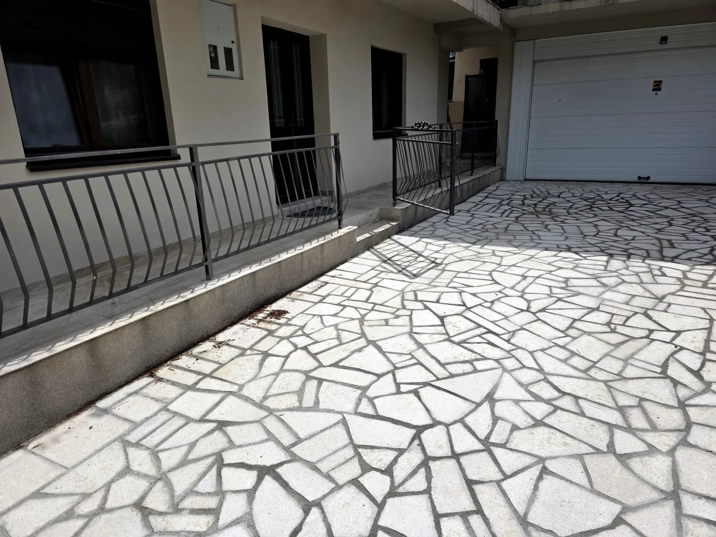 Pogled na popločano dvorište i ulaz u kuću sa garažom.