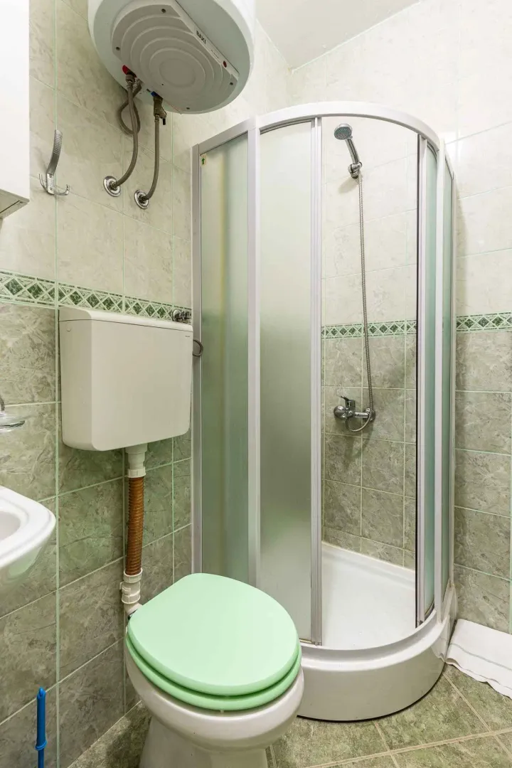 Kupatilo sa tuš kabinom, WC šoljom i bojlerom na zidu.