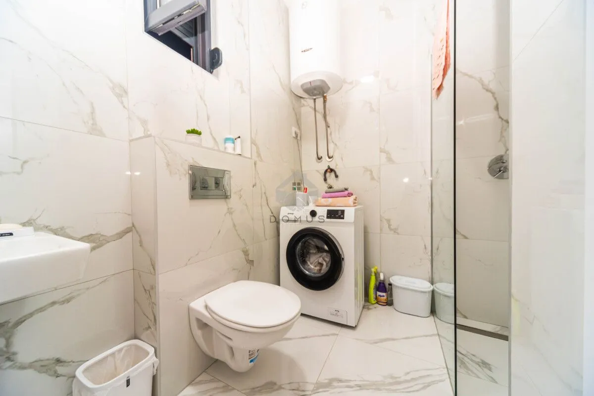 Moderne kupatilo sa tuš kabinom, wc šoljom, umivaonikom i veš mašinom.