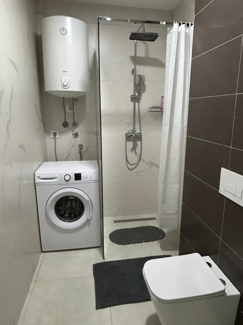 Smaller bathroom with a walk-in shower, toilet, washing machine, and water heater.