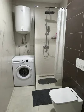 Smaller bathroom with a walk-in shower, toilet, washing machine, and water heater. - image 6