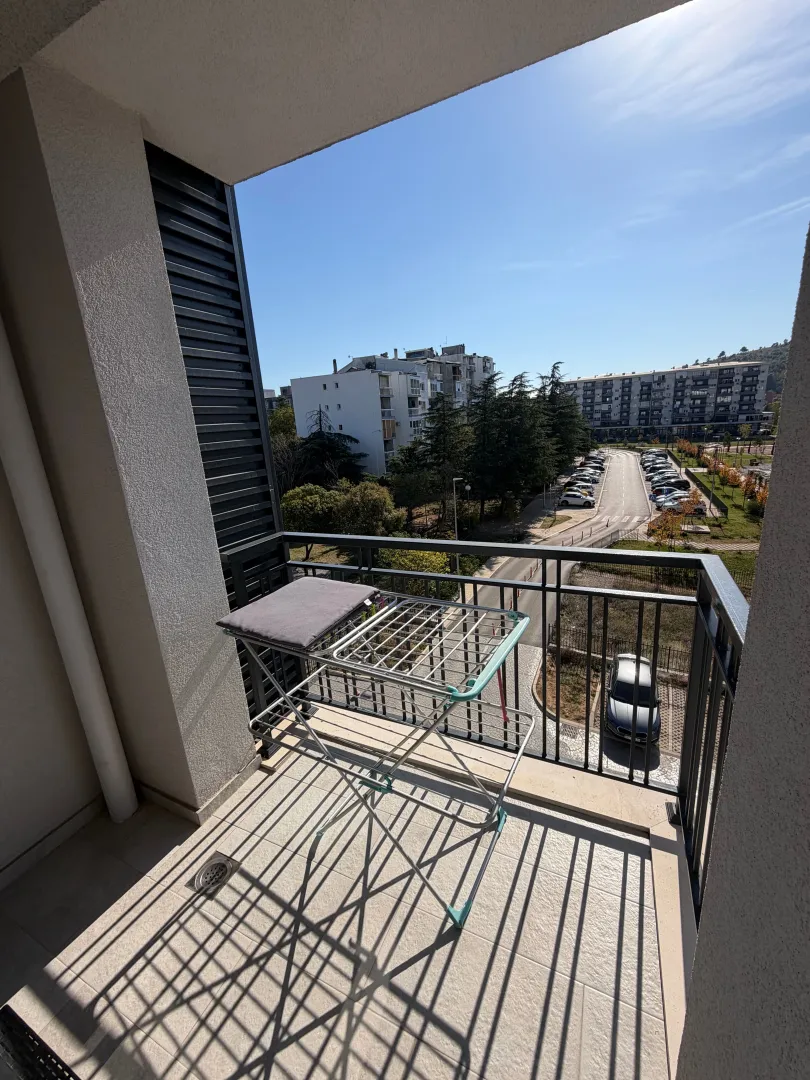 Covered balcony with a clothes drying rack and a view of surrounding buildings and parking.