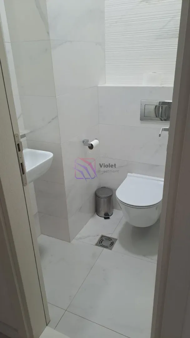 Smaller bathroom with white tiles, washbasin and toilet bowl.