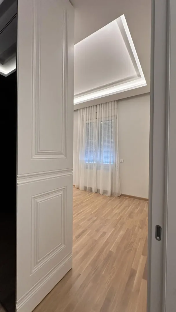 Pogled iz hodnika kroz otvorena vrata na praznu prostoriju sa parketom i spuštenim plafonom.
