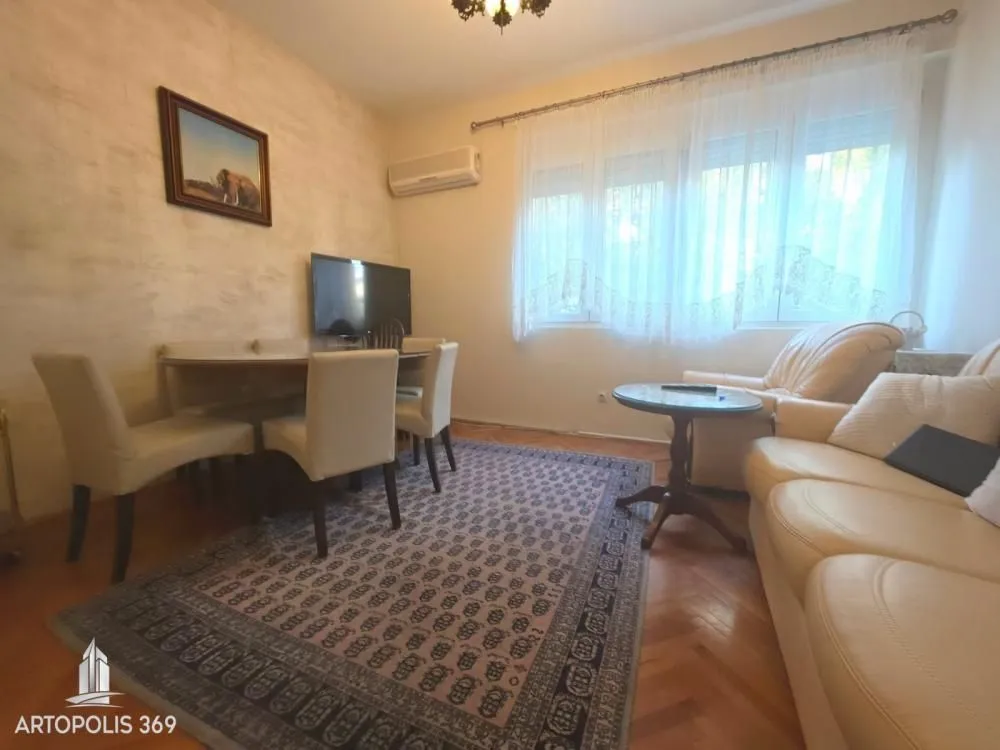Dnevna soba sa garniturom za sedenje, trpezarijskim stolom i prozorima.