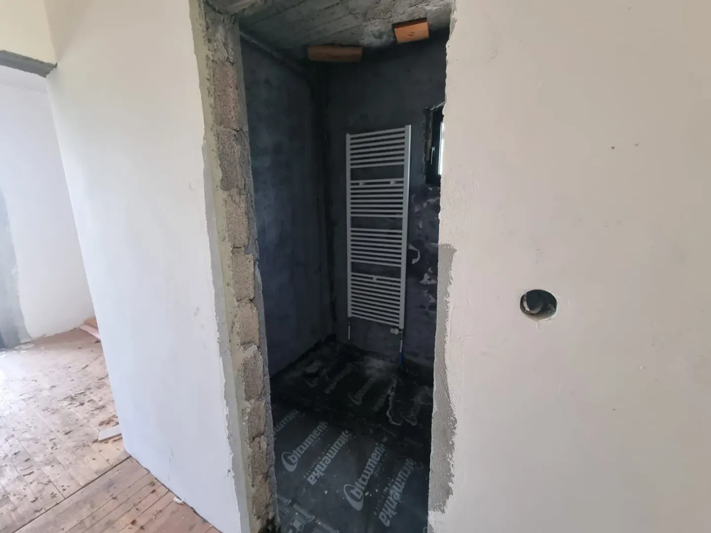 Prostorija u sivoj fazi gradnje sa instaliranim zidnim radijatorom.