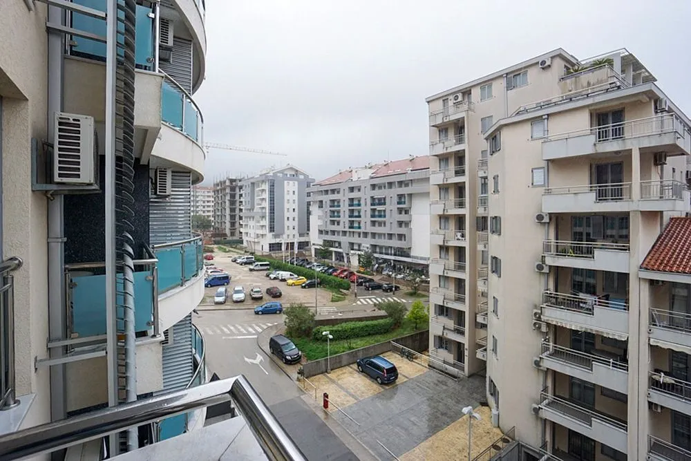 Pogled sa balkona na okolne stambene zgrade i parking.