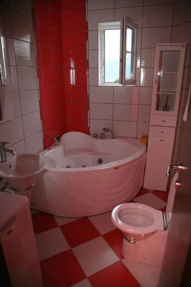Kupatilo opremljeno ugaonom kadom, umivaonikom, toaletom i bijelim ormarićem.