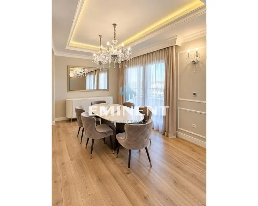 Prostrana trpezarija sa modernim stolom, stolicama i elegantnim lusterom.