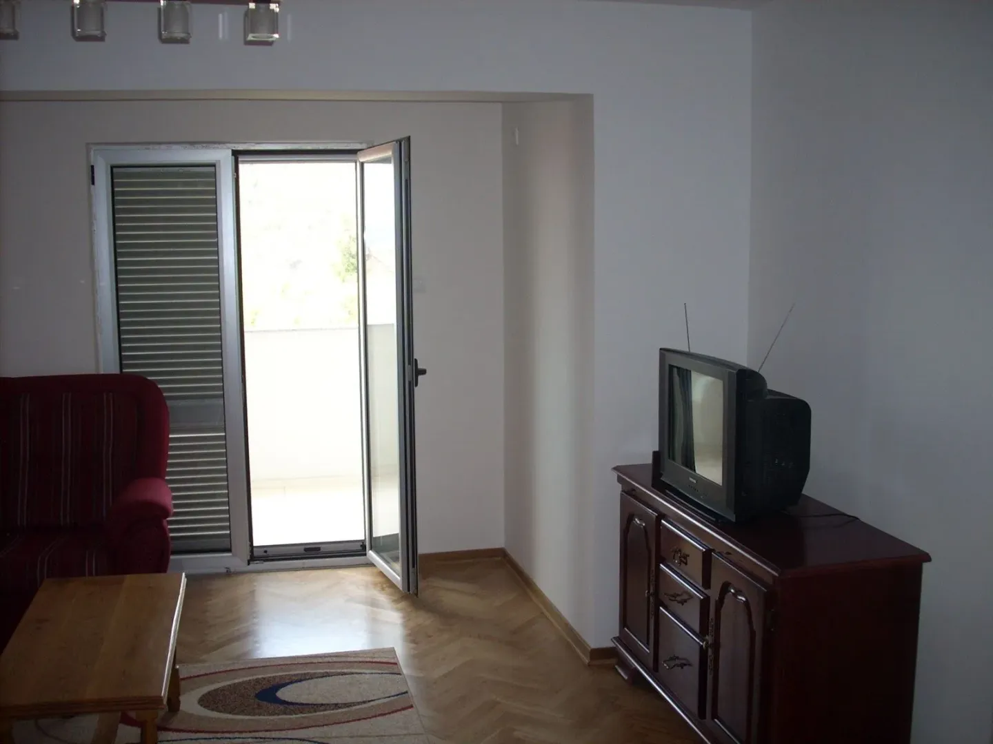 Jednostavno namještena dnevna soba sa izlazom na balkon i parketom.