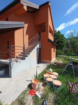 Eksterijer kuće narandžaste fasade sa spoljnim stepeništem i građevinskim materijalom u dvorištu. - image 11