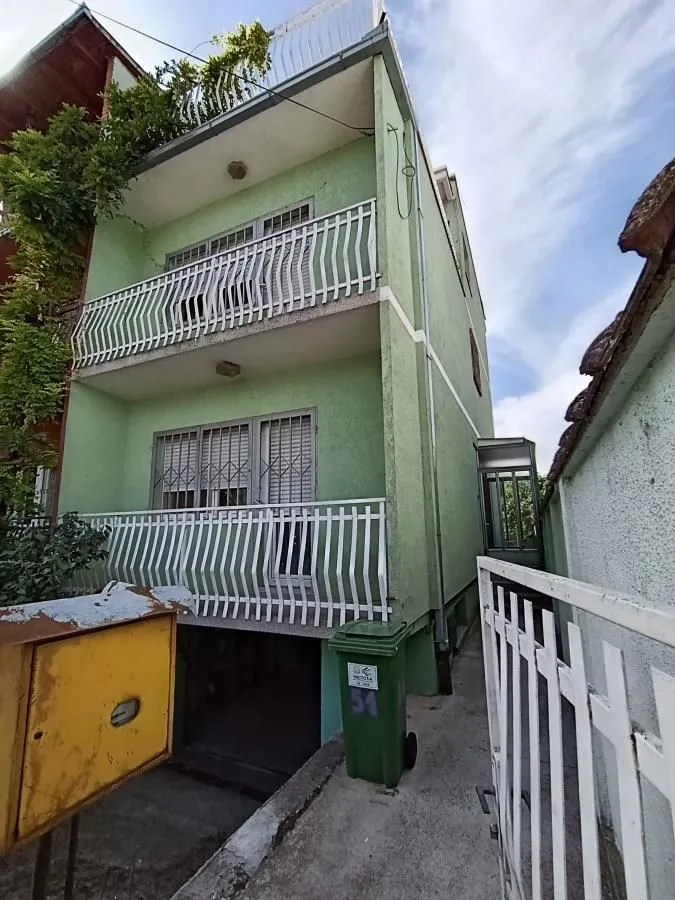 Pogled na spoljašnjost trospratne kuće sa balkonima i zelenom fasadom.