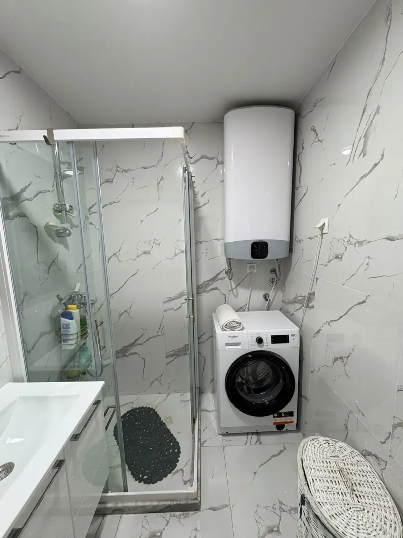 Moderne kupatilo sa tuš kabinom, umivaonikom i veš mašinom.