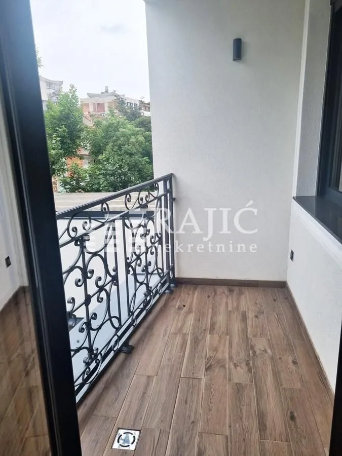 Small enclosed balcony with wooden flooring and wrought iron railing.