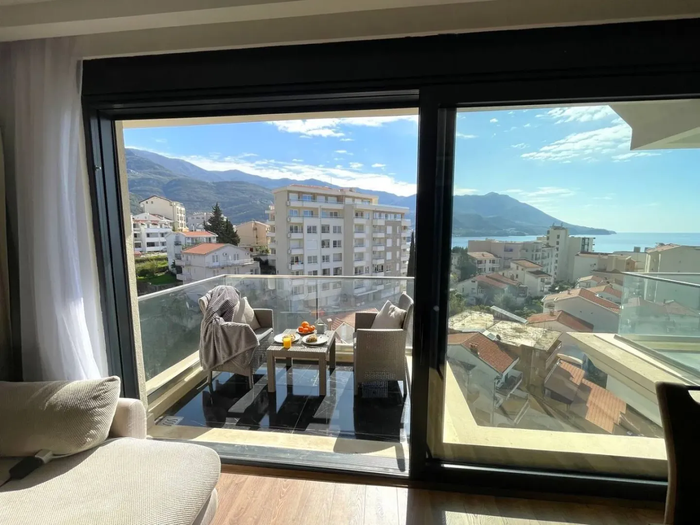 View from the room onto a furnished balcony with seating furniture and a view of the city and sea.