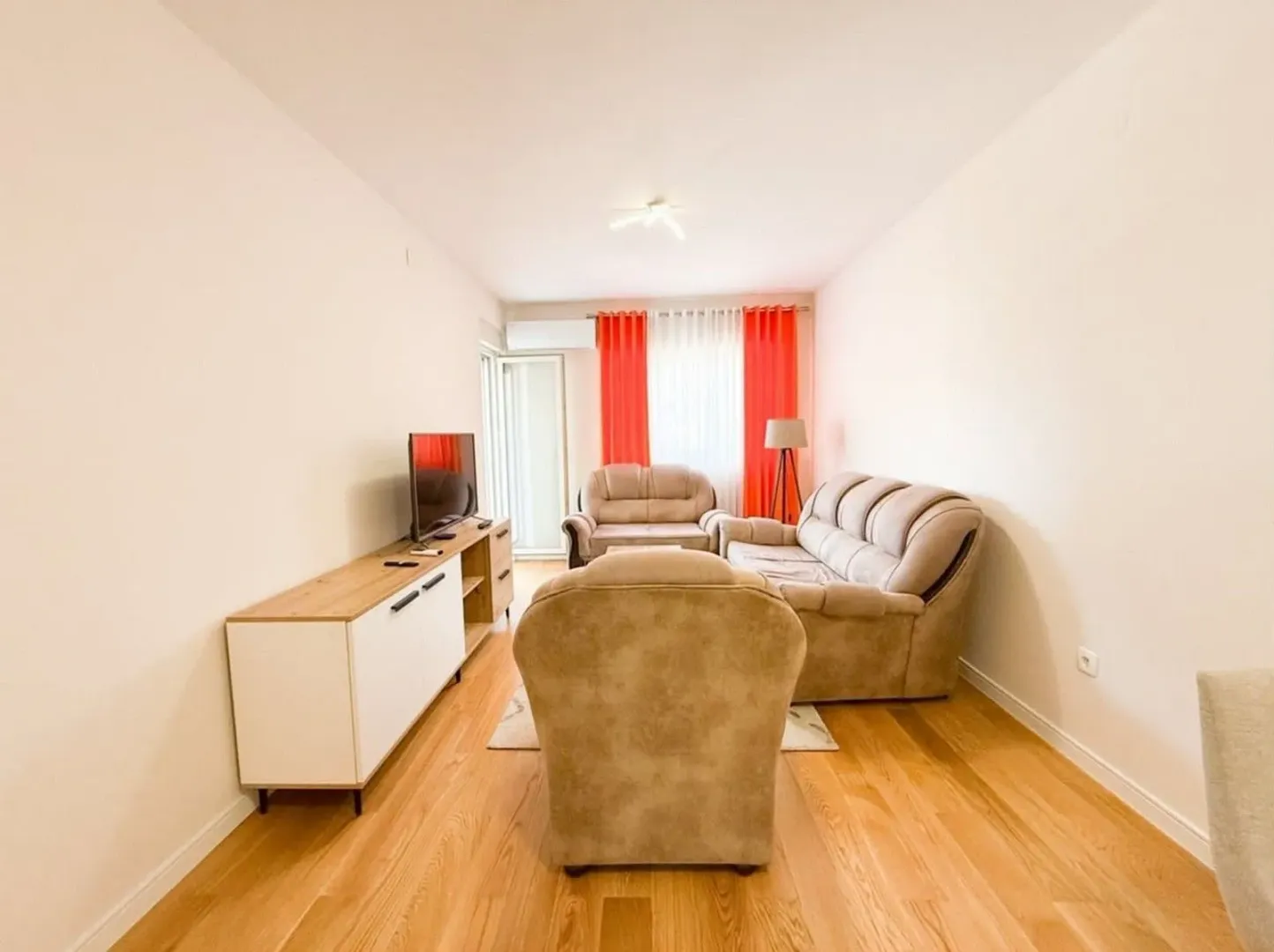 Living room with seating furniture, TV unit, and hardwood flooring.