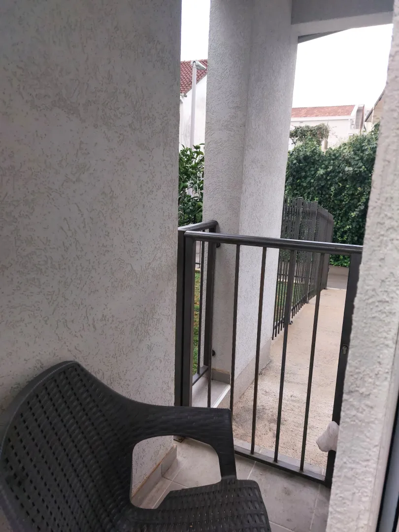 Covered terrace with a black plastic chair and a view of the yard.
