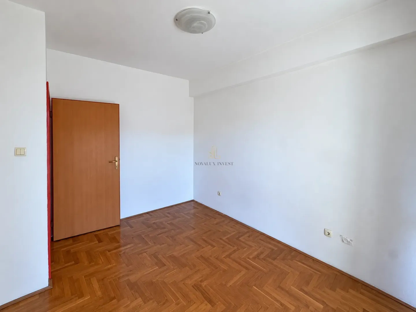 Empty room with wooden parquet flooring and a closed wooden door.