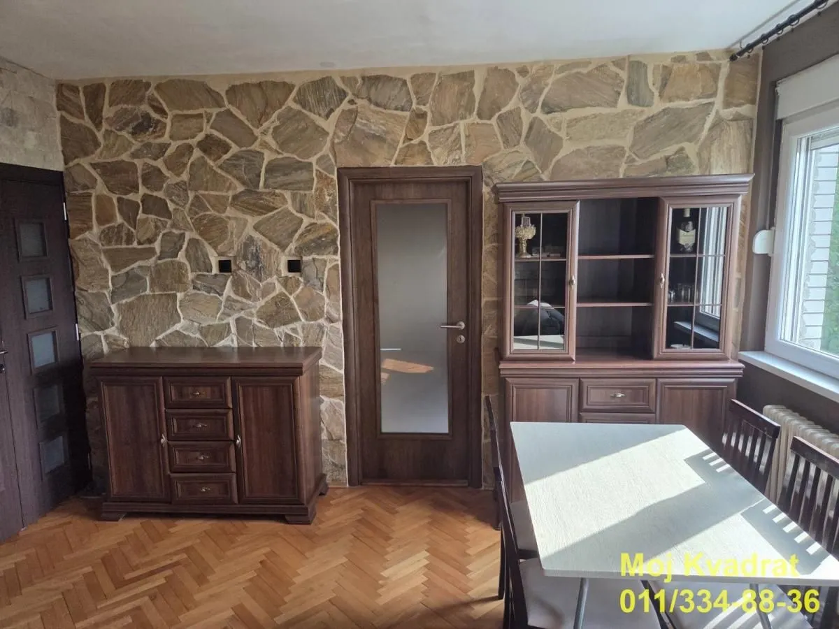 Trpezarija sa drvenim nameštajem i zidom obloženim kamenom.