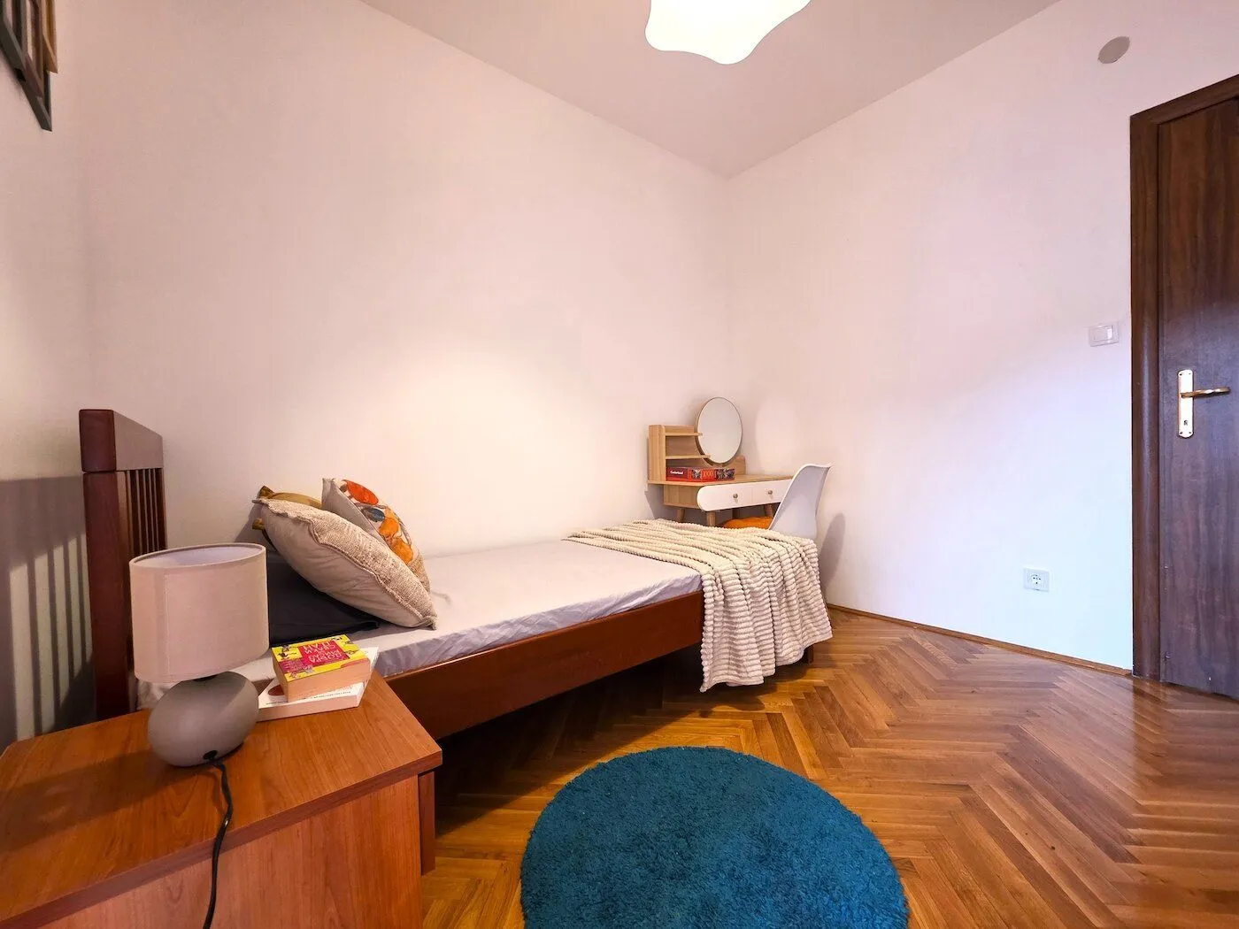 Smaller bedroom with a bed, desk, and parquet flooring.