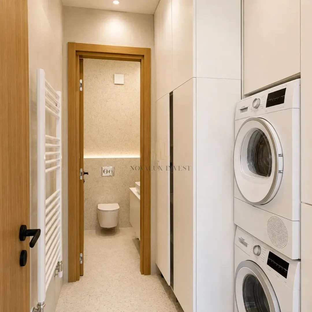 A hallway with built-in closets, a washing machine, and a tumble dryer, with a view of the bathroom.