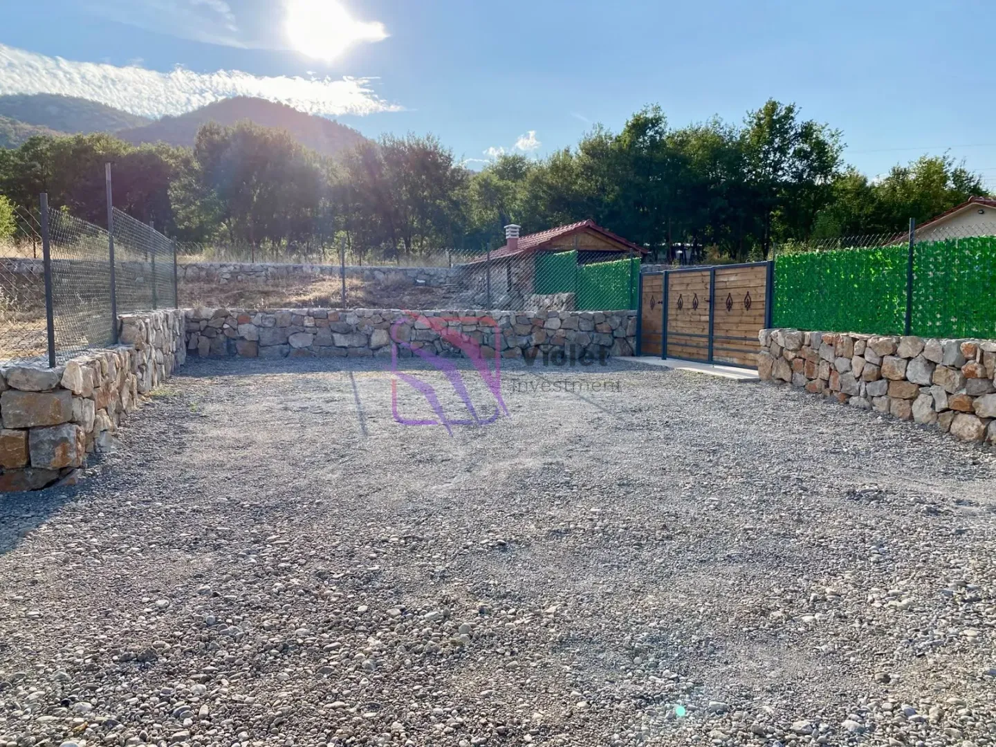 Fenced yard with gravel surface and stone walls.
