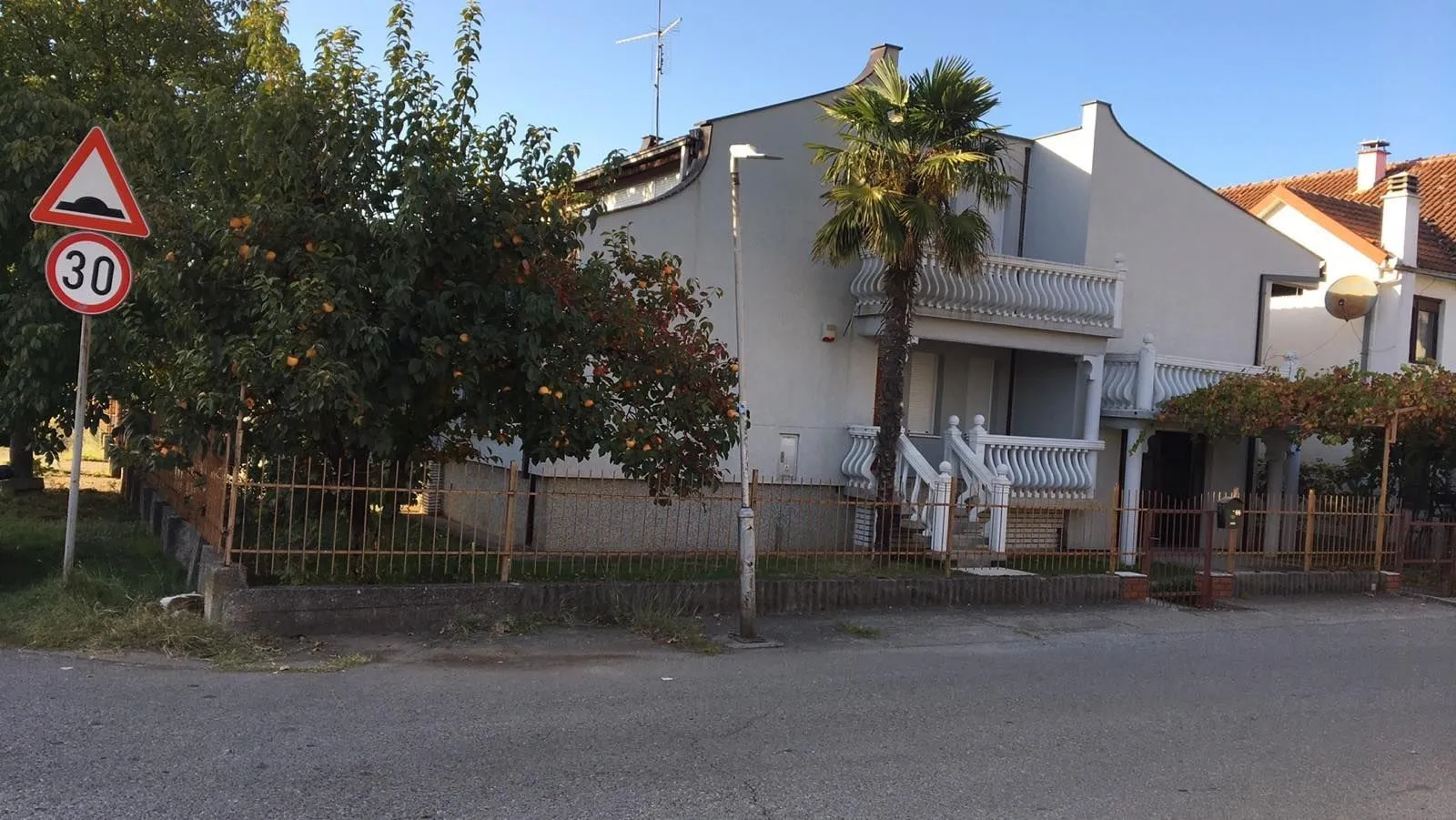 Exterior view of a two-story house with a fenced yard and a palm tree.