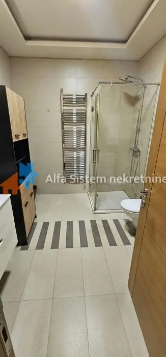Moderno kupatilo sa tuš kabinom, WC šoljom i drvenim ormarićem.
