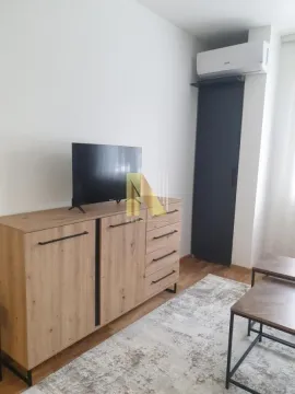 Dnevna soba sa drvenom komodom, televizorom i klima uređajem na zidu. - image 3