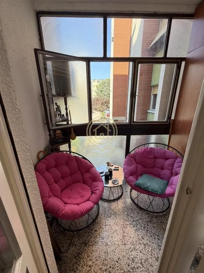 Enclosed balcony with two pink armchairs and a small table.